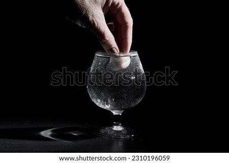 Fingers of hand of a woman touching water or mineral water in a wine glass on black background