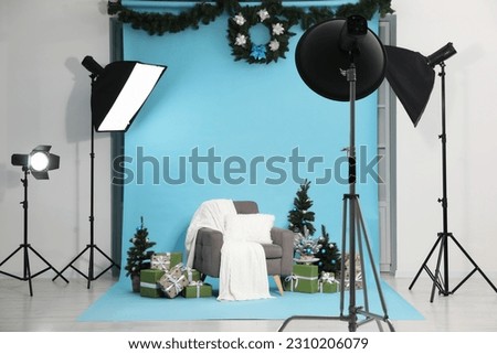 Beautiful Christmas themed photo zone with professional equipment, stylish armchair, trees and gift boxes in studio
