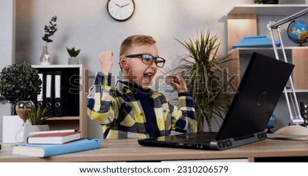 Front view of likable smart modern teen schoolboy in glasses which sitting at the computer at home