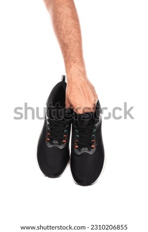 Pair of new unbranded black sport running shoes or sneakers in male hand isolated on white background with clipping path. High quality photo