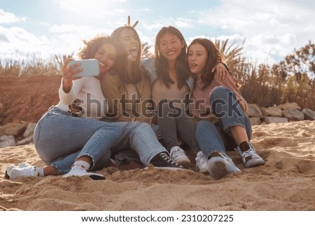 Four young multiracial female friends taking a group selfie while relaxing on the beach beach