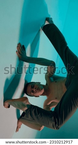 Contemporary dance style. Upside down. Young shirtless man dancing contemp, experimental dance over blue, cyan studio background. Concept of art, body aesthetics, motion, action, inspiration. Royalty-Free Stock Photo #2310212917