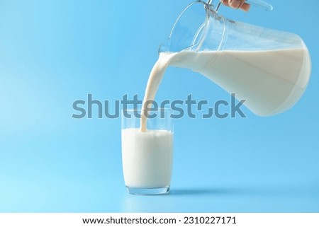 Pouring fresh milk into the glass on light blue background. Royalty-Free Stock Photo #2310227171