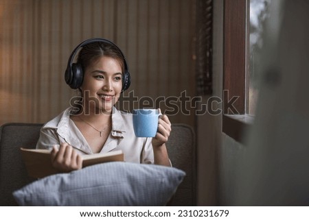 Smiling asian woman reading book at home, relaxing on a couch