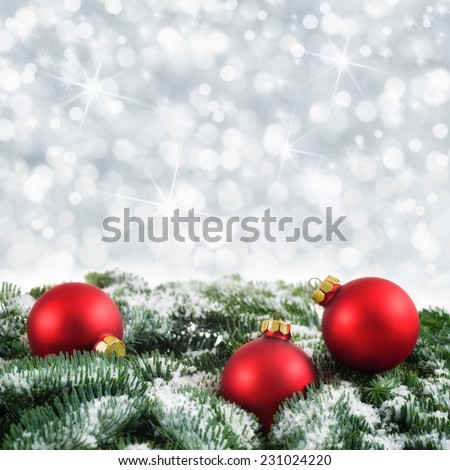 Christmas arrangement with red baubles on snow-covered fir twigs and a silver background of out-of-focus lights