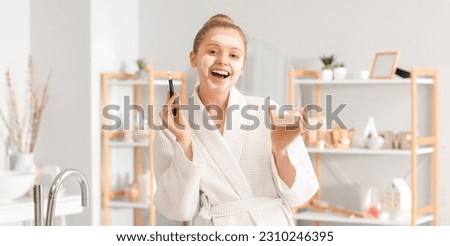 Happy young woman with turmeric mask and brush in bathroom