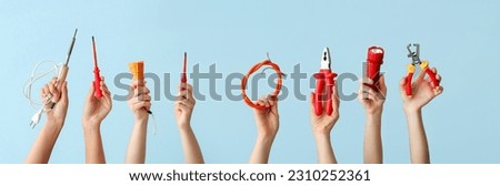 Female hands with set of electrician's supplies on light blue background