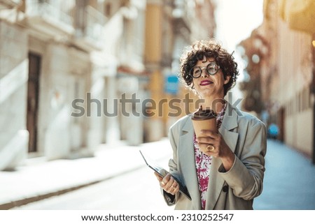 Portrait of a Successful Business woman Using iPad pro. Portrait of smiling young woman walking in city with tablet, drinking takeaway coffee, going down the street with happy expression.