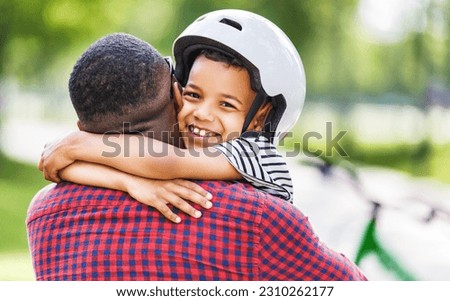 Happy african american boy in helmet hugging dad after cycling together in park
