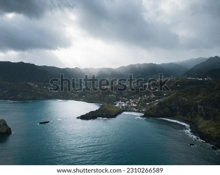 Drone picture of the coastline of Madeira, porto da cruz, cloudy sky with sun rays peaking from the clouds, blue water and green land