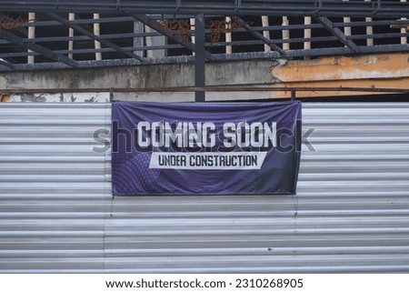 Coming Soon sign banner at the side of the road or intersection, under construction building is in background. Signboard with the words Coming Soon outdoor for brand new hotel soon open.