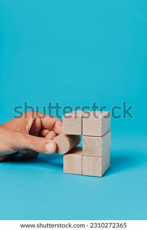 a man puts a cylindrical toy block in a stack of rectangular toy blocks, on a blue background with some blank space on top Royalty-Free Stock Photo #2310272365