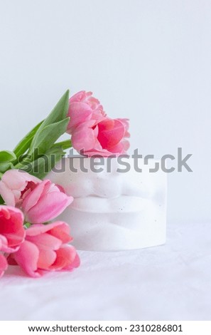Pink tulips bouquet and greek plaster statue lying on white wrinkled blanket background copy space, many spring flowers, gift for woman, greeting card, freshness and blossom, big white gypsum lips