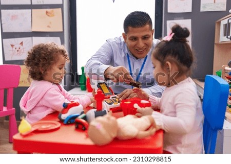 Hispanic man and girls playing supermarket game sitting on table at kindergarten Royalty-Free Stock Photo #2310298815