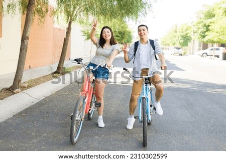 Cheerful beautiful woman and man going on a fun date making the peace sign while going on a ride bike outdoors on a beautiful summer day