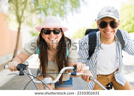 Fun girlfriend and boyfriend with sunglasses and hats smiling making eye contact and laughing during a bike ride outdoors during summer