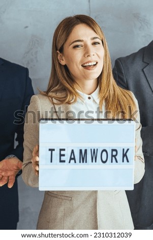 Portrait of multi ethnic successful business team looking at camera in the office and team leader holding sign ''teamwork'' in hands. Group of successful multiethnic business team 