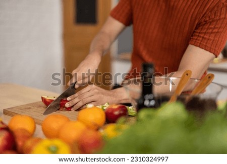 A homely and healthy male prepares nutritious diet, including variety of fruits. Following cooking show on laptop Mastery of peeling, chopping, and slicing fruits to prepare them in artistic style. Royalty-Free Stock Photo #2310324997