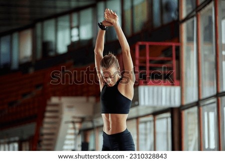 Young athlete girl is warming up before the race at the stadium. A slender blonde in a black tracksuit is concentrating before the competition. Sports and recreation. Half length photo.