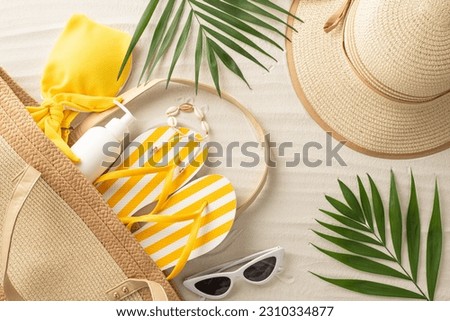 Get beach-ready with picturesque top view of summer essentials: bag with sunglasses, bright flip-flops, woman bodice, sunscreen, bracelet, hat, palm leaves. Your ultimate summer adventure begins here