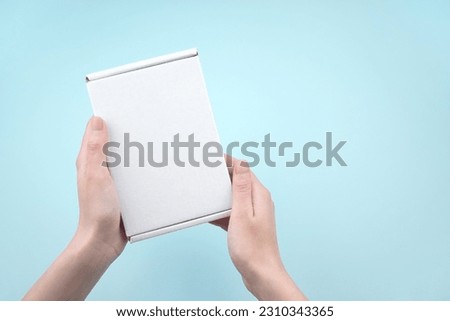 Female hands holding white package box on blue background. Packaging, shopping, delivery concept.