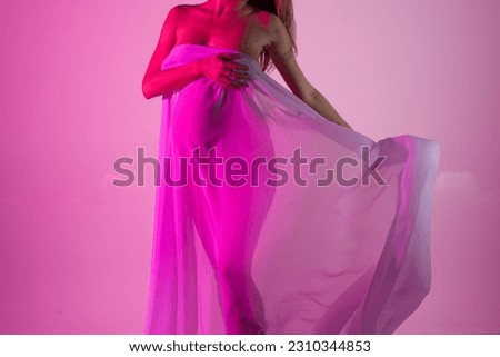 A beautiful pregnant woman in a pink flying dress. Studio pregnancy photo shoot.
