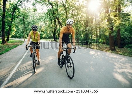 Young couple wearing sportswear and protective helmet while riding bike on a paved road outside of the city. Competition and regular training. Healthy lifestyle concept. Copy space. Royalty-Free Stock Photo #2310347565