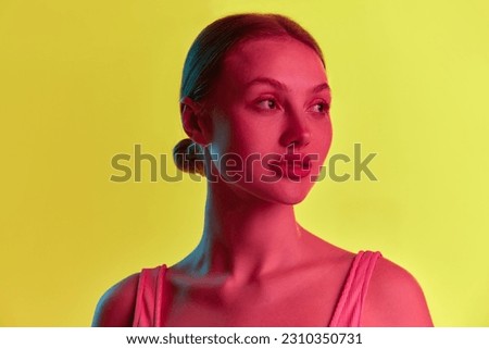 Portrait of young Caucasian girl, student with calm face looking away over yellow-orange background in neon light. Concept of beauty, youth, human emotions, mood, ad