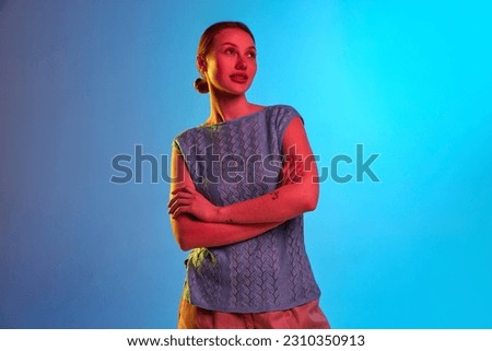 Dreaming, calm. Portrait of pensive girl looking with melancholic facial expression, folding hands and looking away over blue background in neon light. Concept of human emotions, mood, youth, ad Royalty-Free Stock Photo #2310350913