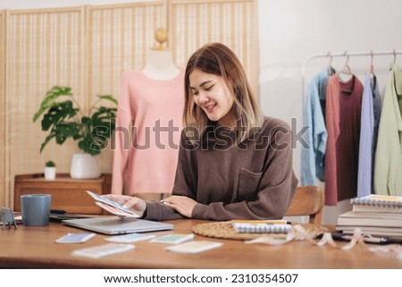Woman designer entrepreneur holding color sample swatch to choosing color while working to sketching design new collection for winter in home workshop.