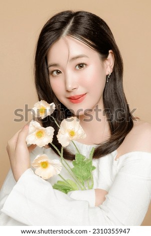 Young Asian beauty woman short hair with korean makeup style on face and perfect clear fresh skin holding flower on isolated beige background. Facial treatment, Cosmetology, plastic surgery.