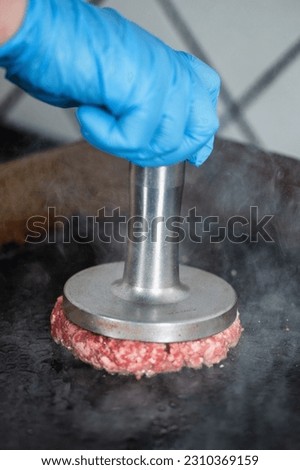 Preparing burger patties on the grill using burger smasher Royalty-Free Stock Photo #2310369159