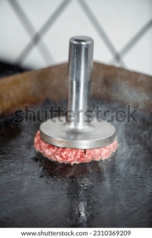 Preparing burger patties on the grill using burger smasher Royalty-Free Stock Photo #2310369209