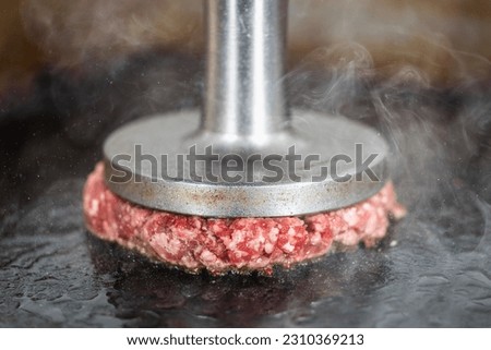 Preparing burger patties on the grill using burger smasher Royalty-Free Stock Photo #2310369213