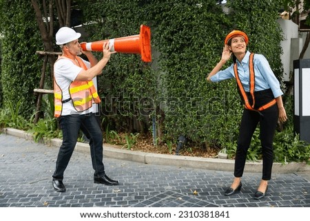Engineer senior man shouting through traffic cone with girlfriend. funny under construction