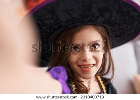 Adorable hispanic girl wearing witch costume making selfie picture by camera at home