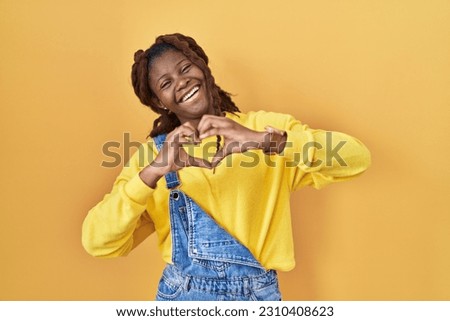 African woman standing over yellow background smiling in love doing heart symbol shape with hands. romantic concept. 