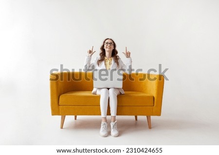 young businesswoman in suit uses laptop on comfortable soft sofa and shows up on copy space, girl in formal wear is typing on computer on yellow couch on white isolated background