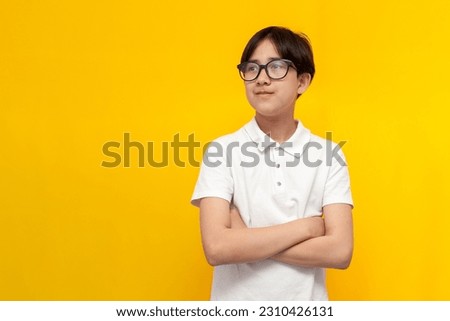 asian smart boy of twelve years old wearing glasses and white t-shirt stands with his arms crossed and looks to the side on yellow isolated background, korean child schoolboy looks at copy space Royalty-Free Stock Photo #2310426131