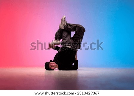 young guy hiphop performer break dance in neon club lighting and doing acrobatic trick, male dancer stands in acrobatic pose