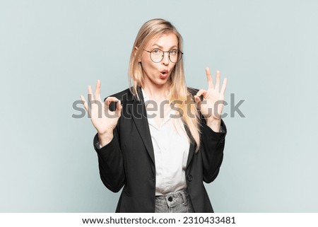 young pretty businesswoman feeling shocked, amazed and surprised, showing approval making okay sign with both hands