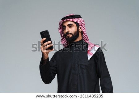 Handsome arab middle-eastern saudi arabian man with traditional saudi clothing in studio - Arabic muslim adult male businessman wearing thwab portrait isolated on gray background Royalty-Free Stock Photo #2310435235
