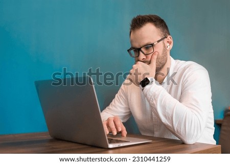 Attractive guy young European businessman works in a laptop sitting at a table in a cafe.