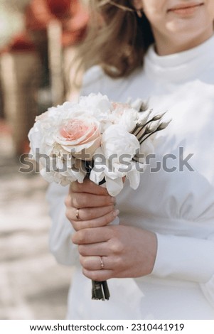 young beautiful caucasian bride holds white wedding bouquet in hands smiling, cropped image, vertical photo, just married, happy newlyweds, love and tenderness, family happiness concept