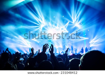 Large group of happy people enjoying rock concert, clapping with raised up hands, blue lights from the stage, new year celebration concept Royalty-Free Stock Photo #231048412