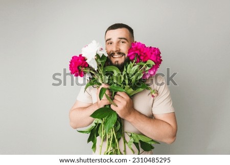 image of a handsome man with a bouquet of pink peonies as a gift. Smiling man with flowers, isolated on a gray background.