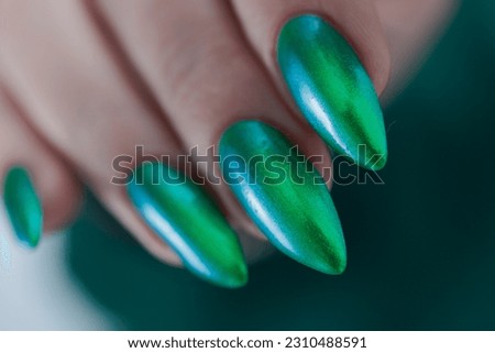 Female hand with long nails and bright green manicure with bottles of nail polish