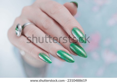 Female hand with long nails and bright green manicure with bottles of nail polish