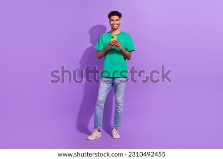 Full size cadre of young smiling blogger guy wear green t-shirt denim jeans hold phone browsing twitter isolated on purple color background