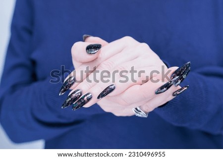 Woman's beautiful hand with long nails and dark blue manicure with bottles of nail polish